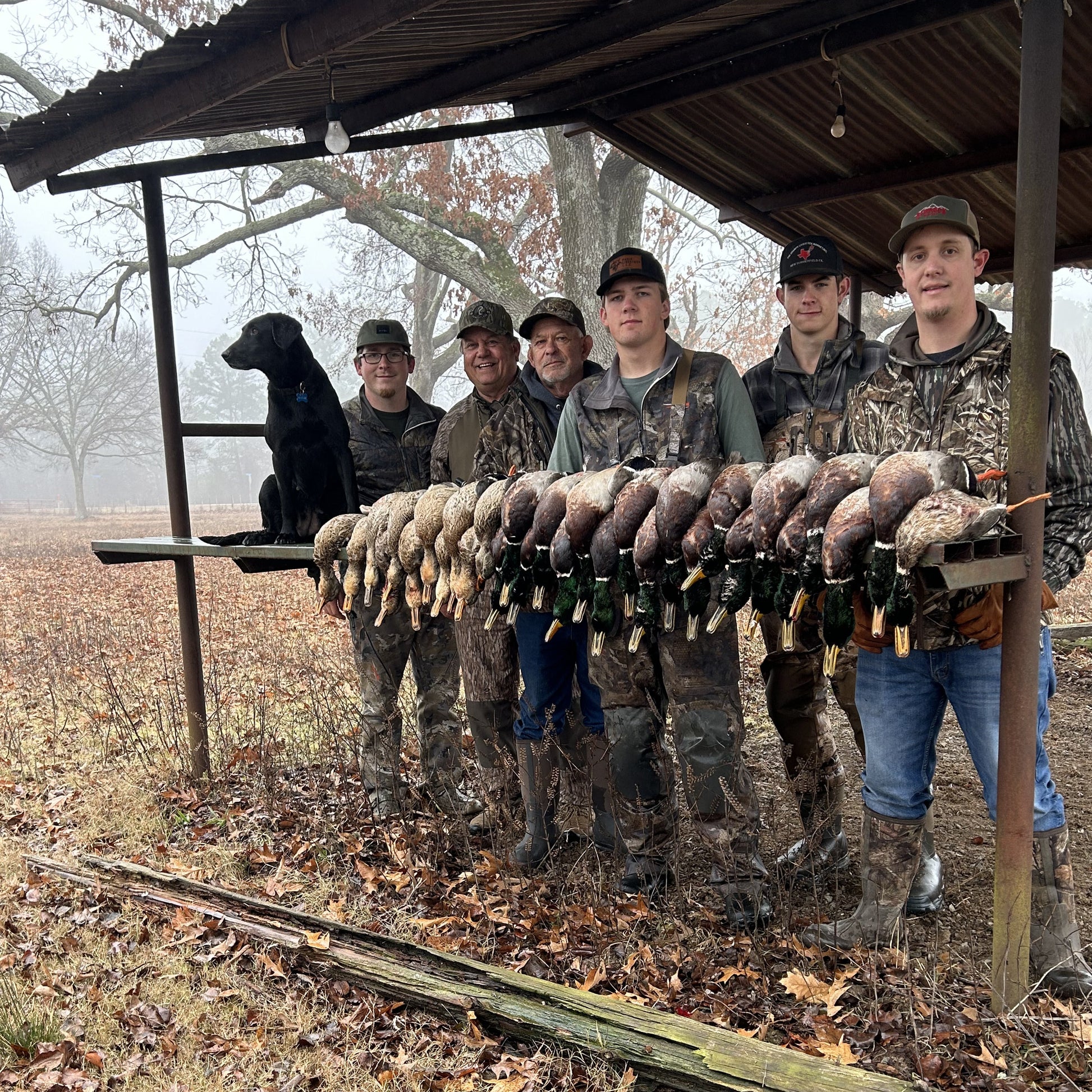 Group of hunters with a lineup of hunted birds under a wooden shelter in a wooded area. Guided waterfowl hunting, duck hunting guide, Texas waterfowl guide service, Oklahoma waterfowl guide service